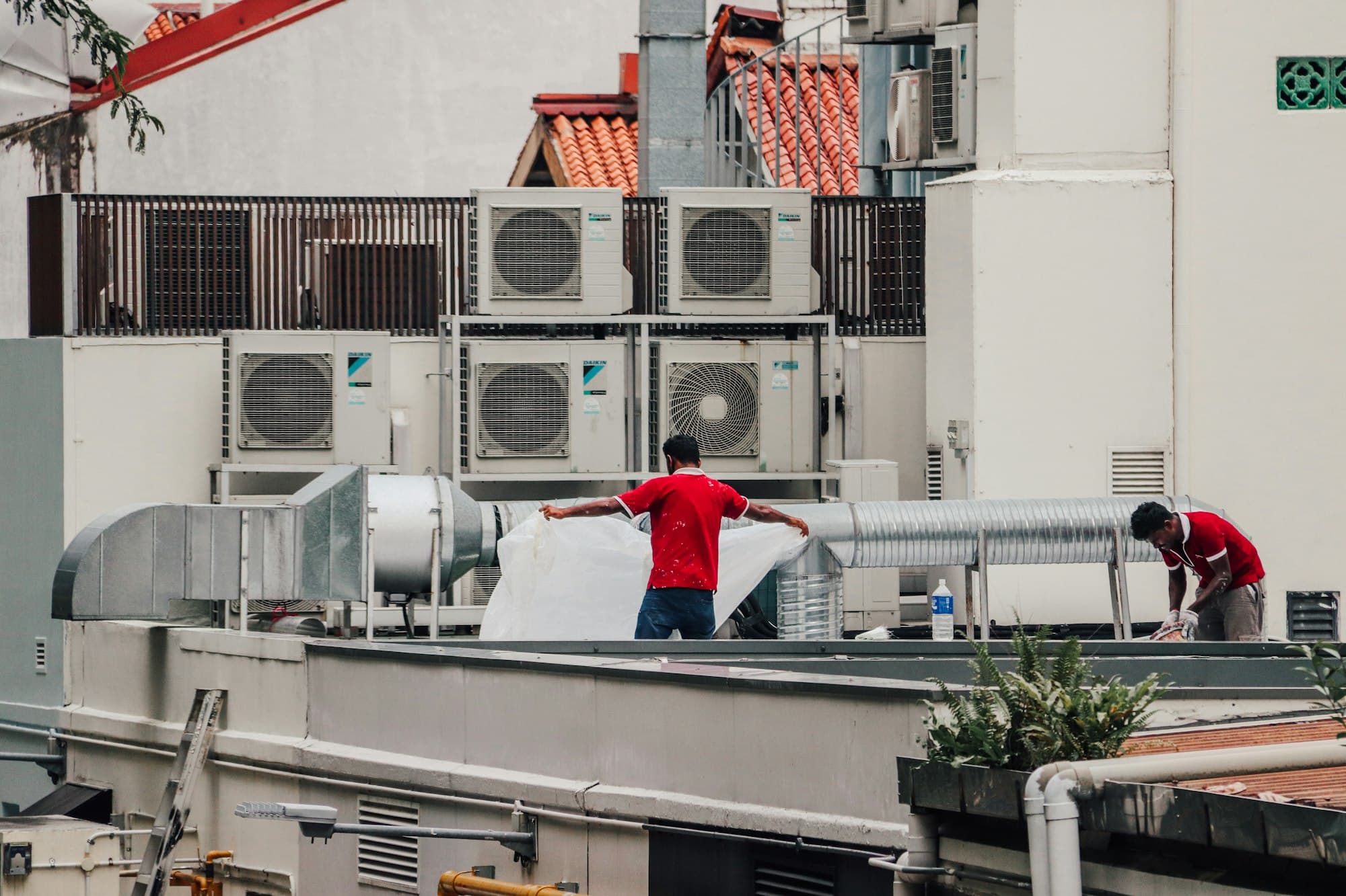 Deux techniciens au travail sur un toit, devant des groupes extérieurs et des gaines de ventilation